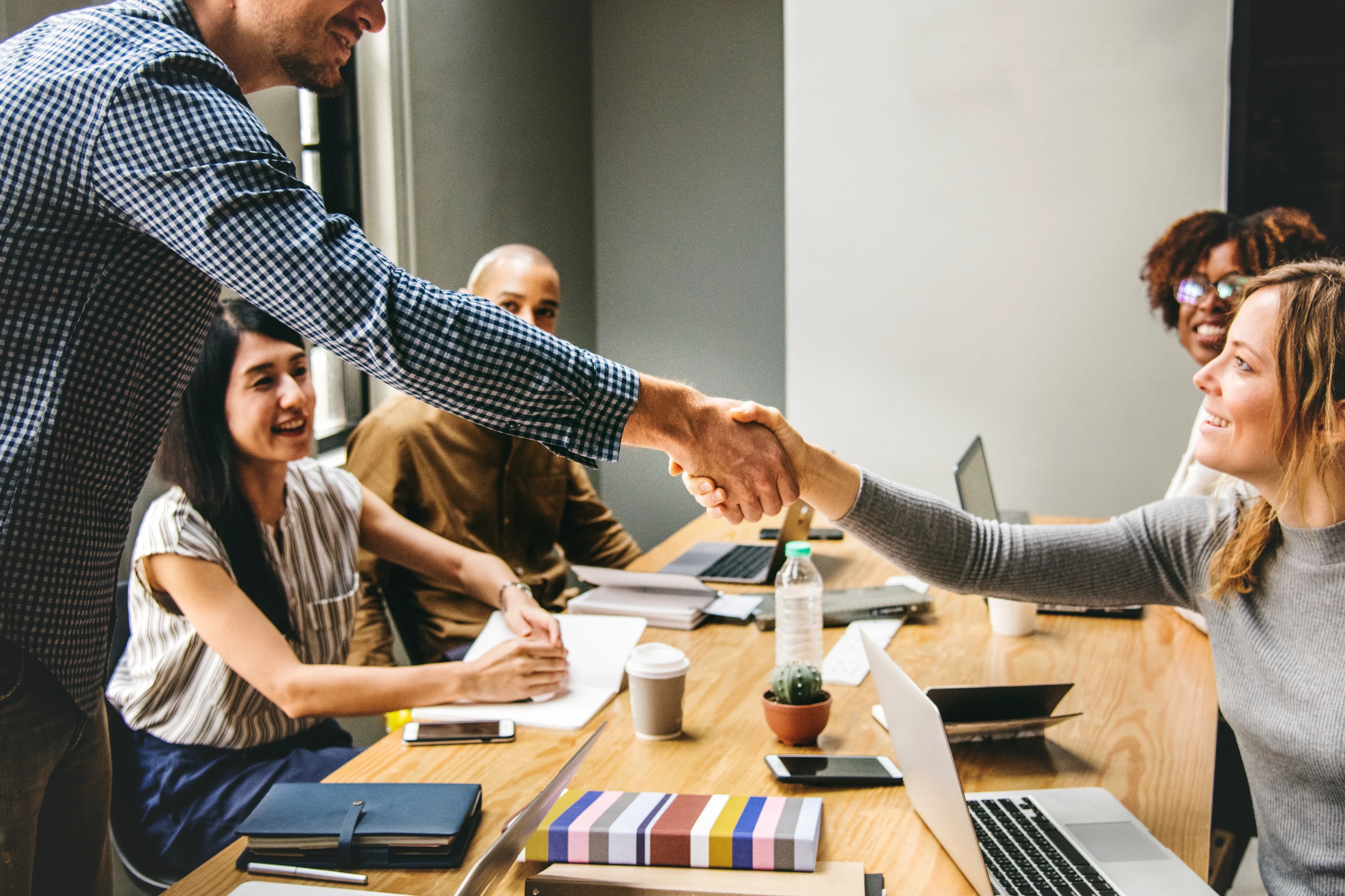 Image: A man and woman shaking hands in an office in front of three other people.