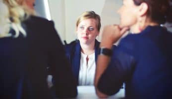 An image of a woman with weary look on her face as she sit across a table from two others.