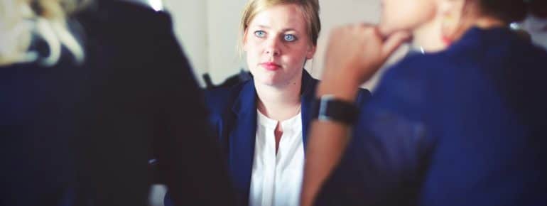 An image of a woman with weary look on her face as she sit across a table from two others.