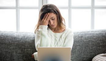 An image of a woman visibly frustrated sitting with her laptop on her couch.