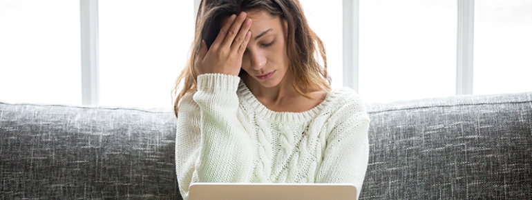 An image of a woman visibly frustrated sitting with her laptop on her couch.