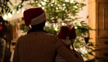 Adult sitting in front of Christmas tree with child.