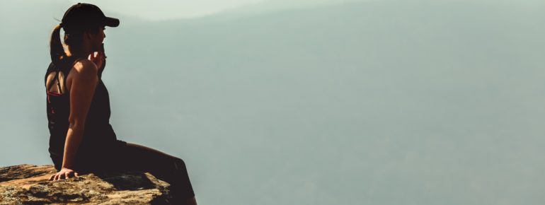 Hiker sitting on cliff looking into the distance.