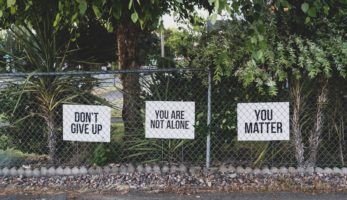 an image of three signs behind a chain-link fence that say, "don't give up, you are not alone, and you matter".