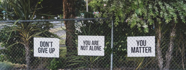 an image of three signs behind a chain-link fence that say, "don't give up, you are not alone, and you matter".
