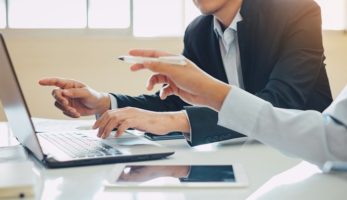 image: Two individuals pointing at something on a laptop screen and discussing