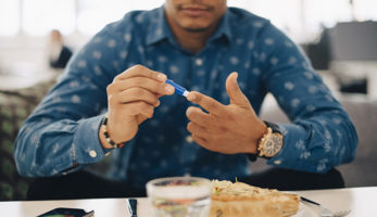 image: Man pricking his finger, doing blood test while sitting in front of his food