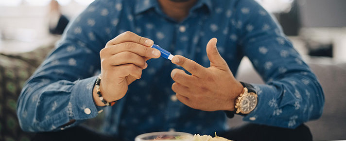 image: Man pricking his finger, doing blood test while sitting in front of his food