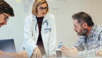 image: Doctor speaking to a patient while two other medical professionals take notes and listen