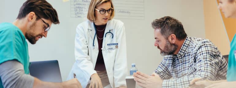 image: Doctor speaking to a patient while two other medical professionals take notes and listen