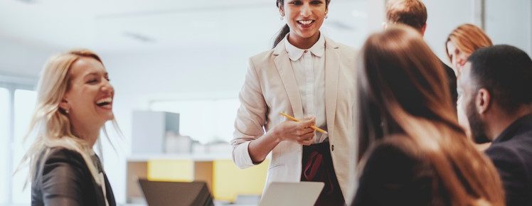 image: Group of business professionals chatting, smiling, laughing, while typing on their computers