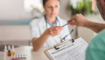 image: Doctor giving a staff member a pen to fill out a Health Insurance Claim Form