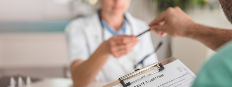 image: Doctor giving a staff member a pen to fill out a Health Insurance Claim Form