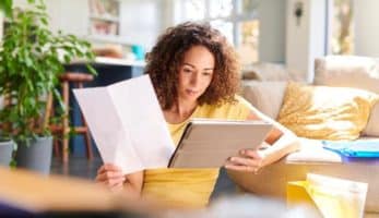 image: Woman looking at a tablet in her hand while holding a document in another