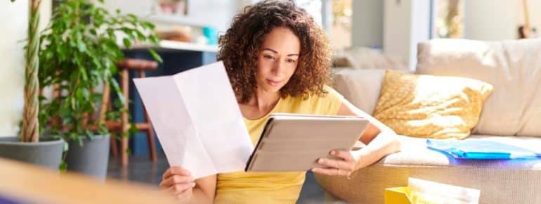 image: Woman looking at a tablet in her hand while holding a document in another