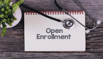 image: notebook with the words "open enrollment" written on it with a stethoscope laid on top of the book