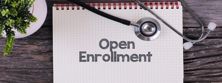 image: notebook with the words "open enrollment" written on it with a stethoscope laid on top of the book
