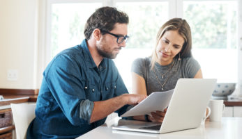 image: Man and woman looking over a document together in front of a laptop