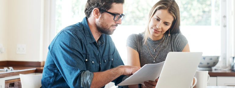 image: Man and woman looking over a document together in front of a laptop