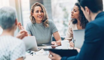 image: Woman smiling while talking to a group of people sitting at her table