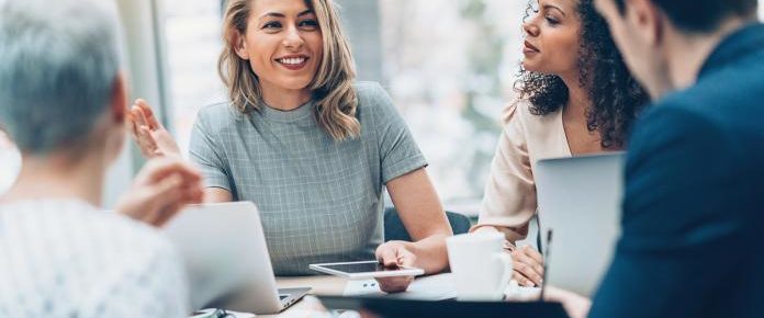 image: Woman smiling while talking to a group of people sitting at her table