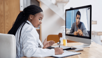 image: Doctor taking notes while speaking to a patient via telehealth