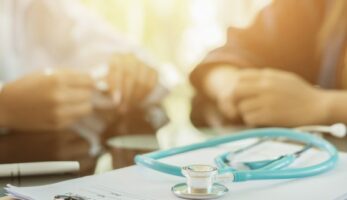 Close up photo of two people discussing healthcare captives at a table with a stethoscope in the foreground.