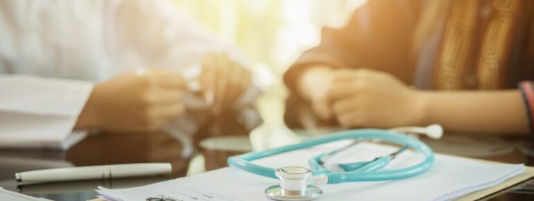 Close up photo of two people discussing healthcare captives at a table with a stethoscope in the foreground.