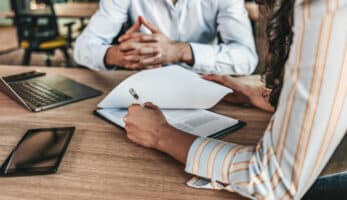 A photo of two pair of hands working at a desk as two people discuss employee benefits.