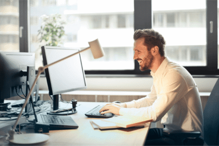 HR professional smiling while managing employee benefits on desktop computer